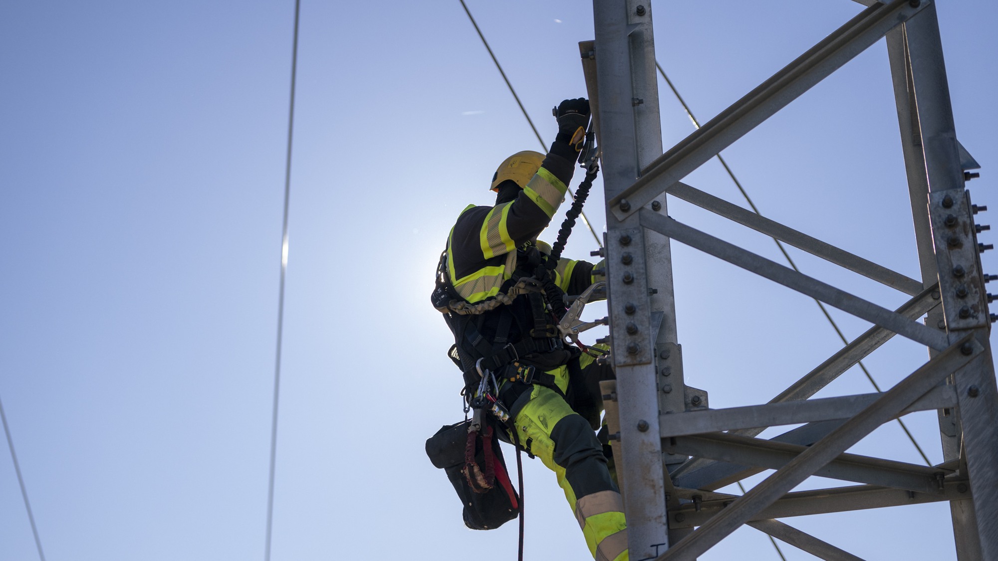 En man i gul skyddsutrustning klättrar upp för en kraftledning.