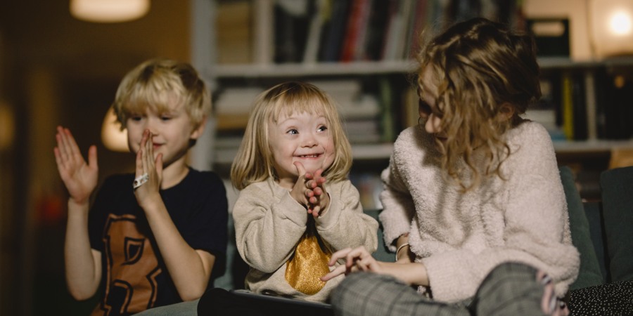 Tre barn sitter i en soffa och klappar.