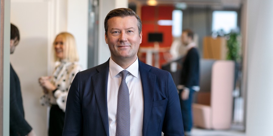 En man i kostym och slips står på ett kontor.